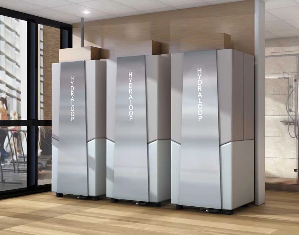 Three Hydraloop water recycling systems installed in a modern indoor space near a bathroom, demonstrating a commercial greywater recycling setup.