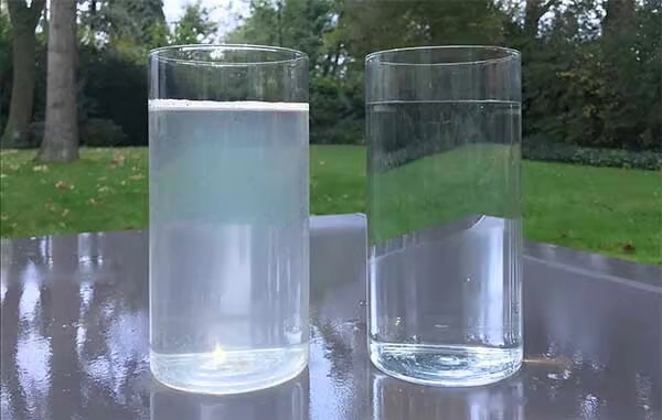 Two clear glasses showing untreated cloudy greywater and filtered clean water side by side on an outdoor table.