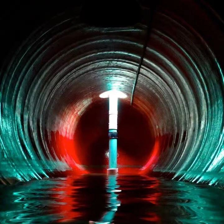 Interior view of a large corrugated water tank with shallow water at the bottom, illuminated by colorful blue and red lighting reflecting off the curved metal walls.
